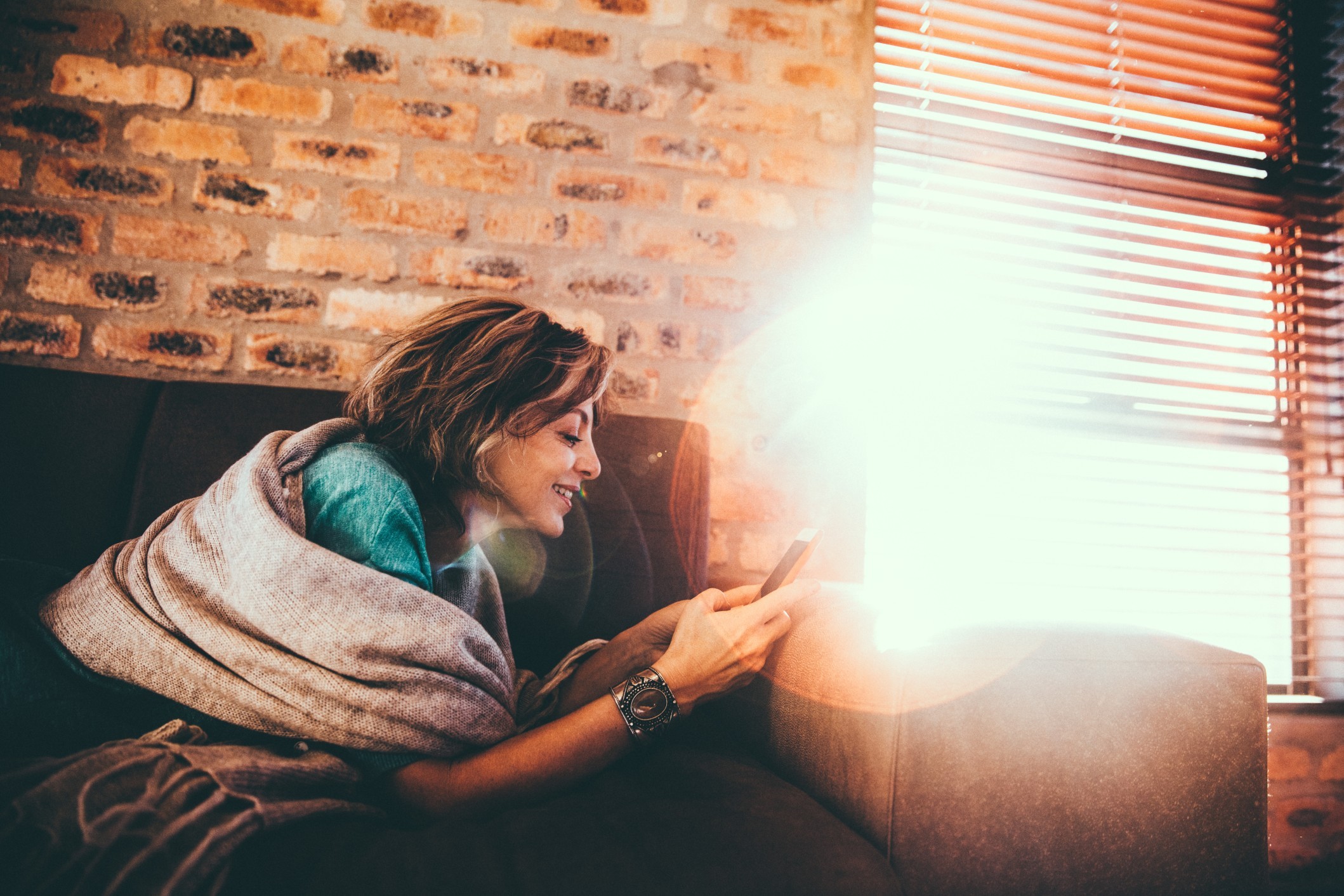 Women using mobile phone on couch at home with sun flare in background t20 Rw6o2w